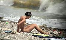 O tipă nud cu părul negru se plimbă goală pe o plajă